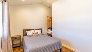 Ein Schlafzimmer mit einem Bett, Nachttischen, einem Holzregal und einem Kleiderhaken.