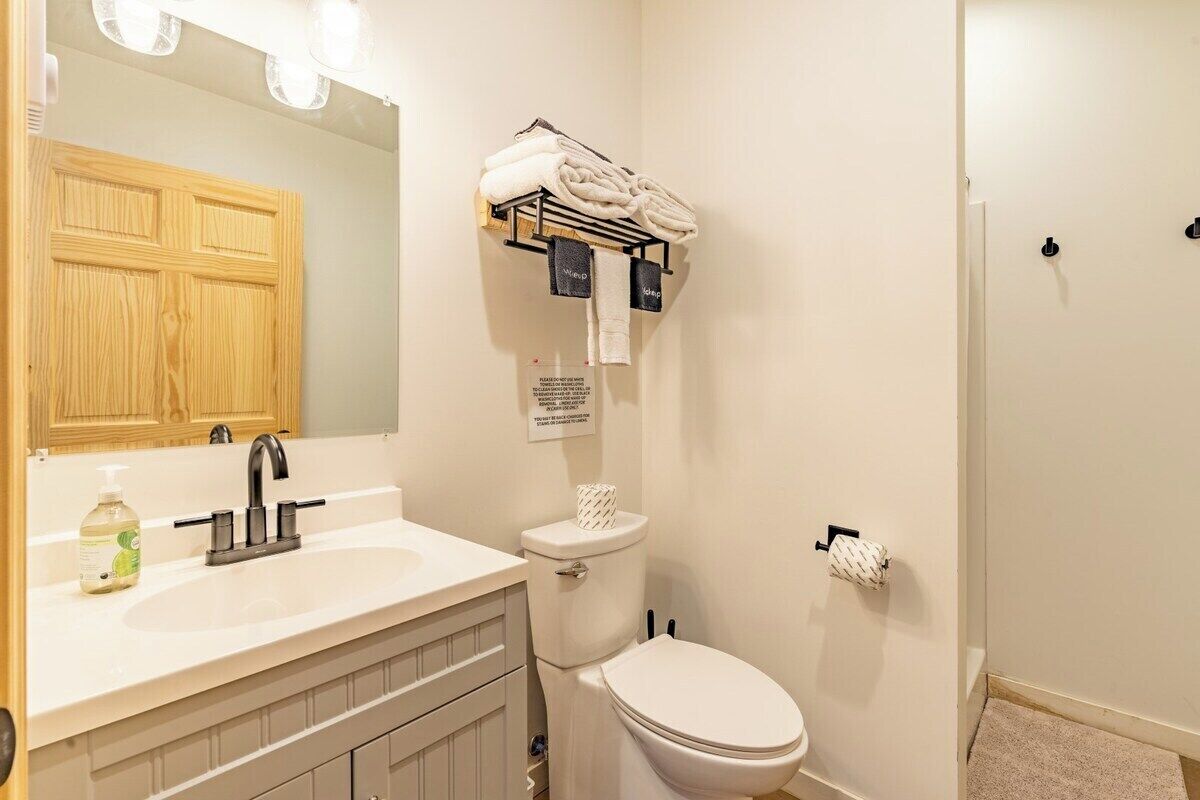 A bathroom with a sink, mirror, towel rack, toilet, and a shower area.