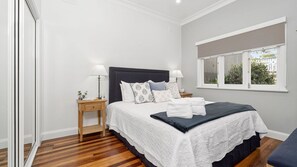 Relax in this serene bedroom with a large bed, pillows, and a window offering a view of lush greenery.