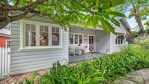 Relax on the front porch with two comfortable chairs and a small table, surrounded by a lush garden.