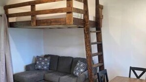 Une pièce comprenant un lit superposé, un canapé, une table à manger avec des chaises et une échelle en bois.
