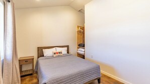 Une chambre à coucher avec un lit, des tables de chevet, une étagère en bois et un porte-manteau suspendu.