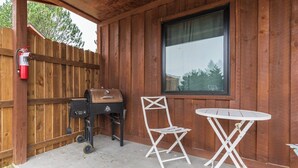 Une terrasse en bois équipée d’un barbecue, d’une chaise pliante et d’une petite table.