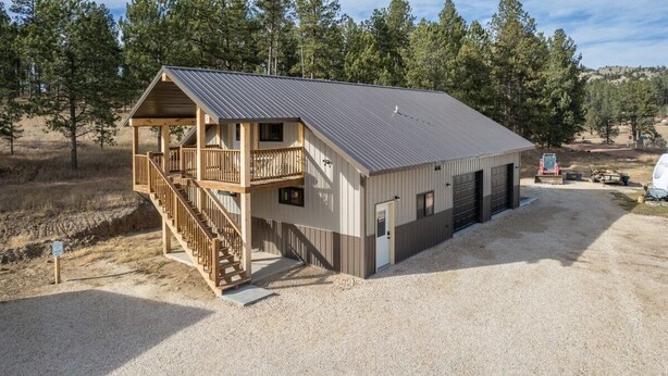 A two-story building with a balcony, a covered porch, and a gravel driveway. - Custer`s Loft at Gold Valley Camp| 1 Bed, 1 Bath (Custer)