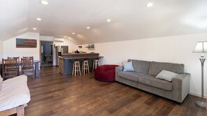 A spacious living area with a sofa, a red bean bag, a dining table with chairs, and a kitchen area with stools. - Custer`s Loft at Gold Valley Camp| 1 Bed, 1 Bath (Custer)