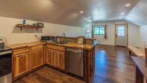 A kitchen with wooden cabinets, a dishwasher, and a microwave. There is a window with a view of greenery outside. - Custer`s Loft at Gold Valley Camp| 1 Bed, 1 Bath (Custer)