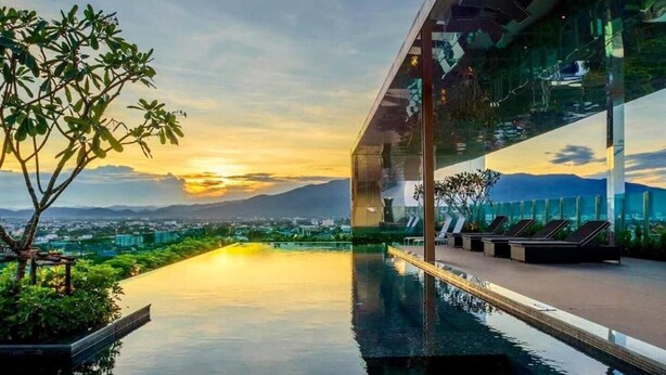 Edifici modern amb piscina all'infinit en la terrassa, amb vista a una ciutat i muntanyes al capvespre.