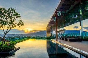 Un bâtiment moderne doté d’une piscine à débordement sur le toit, offrant une vue imprenable sur la ville et les montagnes au coucher du soleil.