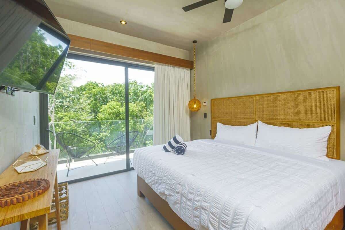 A bedroom with a large bed, a wooden headboard, a ceiling fan, and a view of greenery outside.