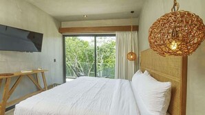 A bedroom with a large bed, a TV mounted on the wall, and a wicker hanging light fixture. - Relaxing 1 BDRM, 1 BR, Balcony & Pool Access Apt (Tulum)