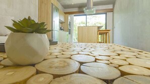 A modern kitchen with a wooden table covered in circular cutouts, a potted plant, and a view of the outdoors. - Relaxing 1 BDRM, 1 BR, Balcony & Pool Access Apt (Tulum)