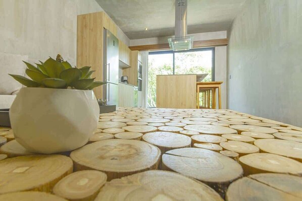 A modern kitchen with a wooden table covered in circular cutouts, a potted plant, and a view of the outdoors.