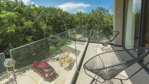 A balcony with a glass railing, two metal chairs, and a view of a red car and trees. - Relaxing 1 BDRM, 1 BR, Balcony & Pool Access Apt (Tulum)