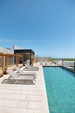 Ein Poolbereich auf dem Dach mit Liegestühlen, einer Holzpergola und freiem Blick auf den Ozean.