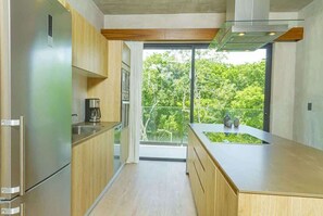 A modern kitchen with wooden cabinets, stainless steel appliances, and a large window overlooking greenery. - Relaxing 1 BDRM, 1 BR, Balcony & Pool Access Apt (Tulum)