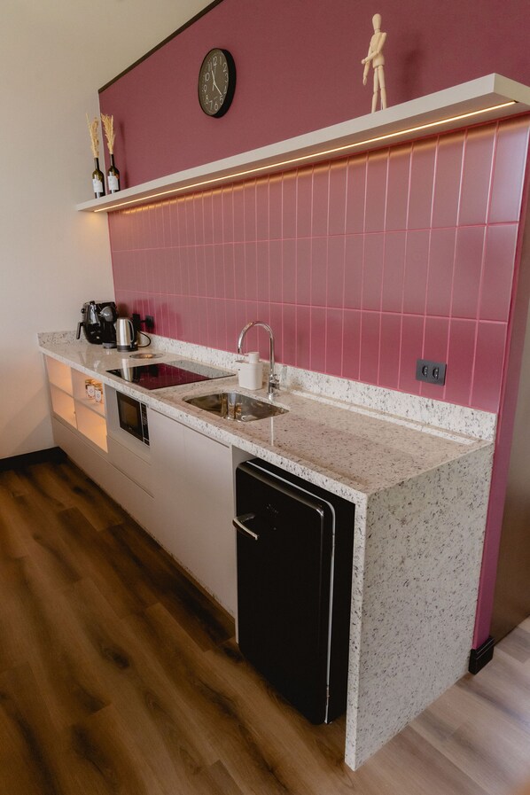 A compact kitchen with a sink, countertop, and a clock on the wall. - Primo Cabana - Hospedagem na Vinícola (Quatro Barras)
