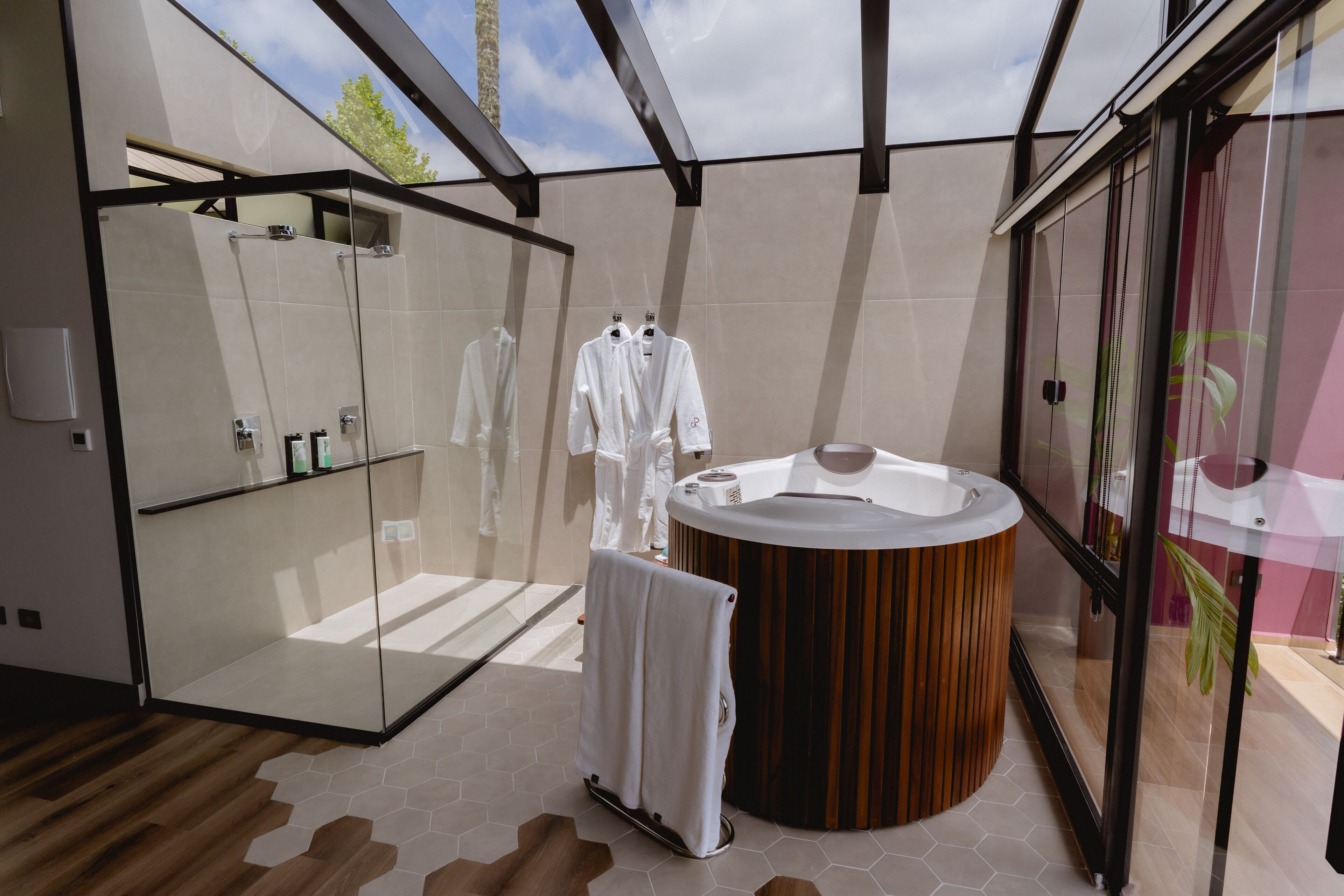A modern bathroom with a glass shower enclosure, a wooden bathtub, and a glass-enclosed vanity.