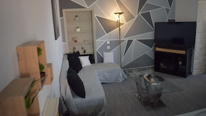 A modern living room with a sofa, a glass coffee table, a TV, and a geometric wall design. - Ethra Casa (Corfu)