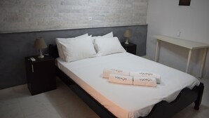 A neatly made bed with white linens and towels, a bedside table with a lamp, and a small bedside table with a phone. - Ethra Casa (Corfu)