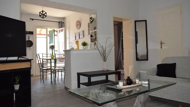A modern living room with a glass coffee table, a sofa, a TV, and a dining area with chairs and a table. - Ethra Casa (Corfu)