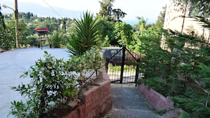 A paved pathway leading to a gated entrance, surrounded by lush greenery and a parked car. - Ethra Casa (Corfu)