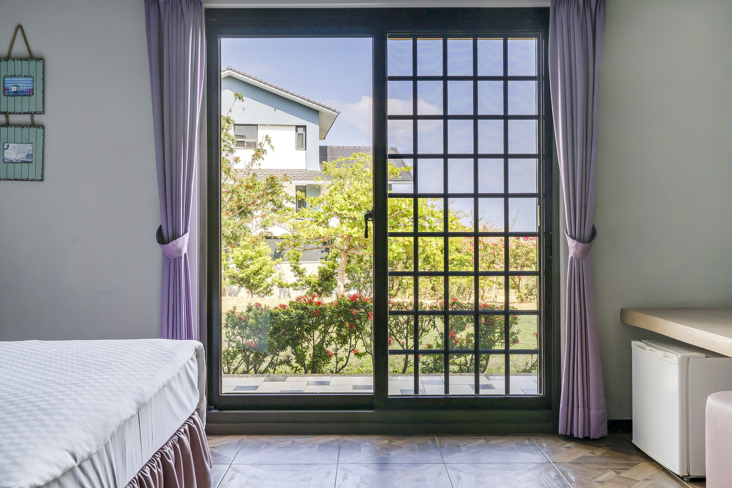 A room with a bed, a window with a view of buildings and greenery, and a radiator.