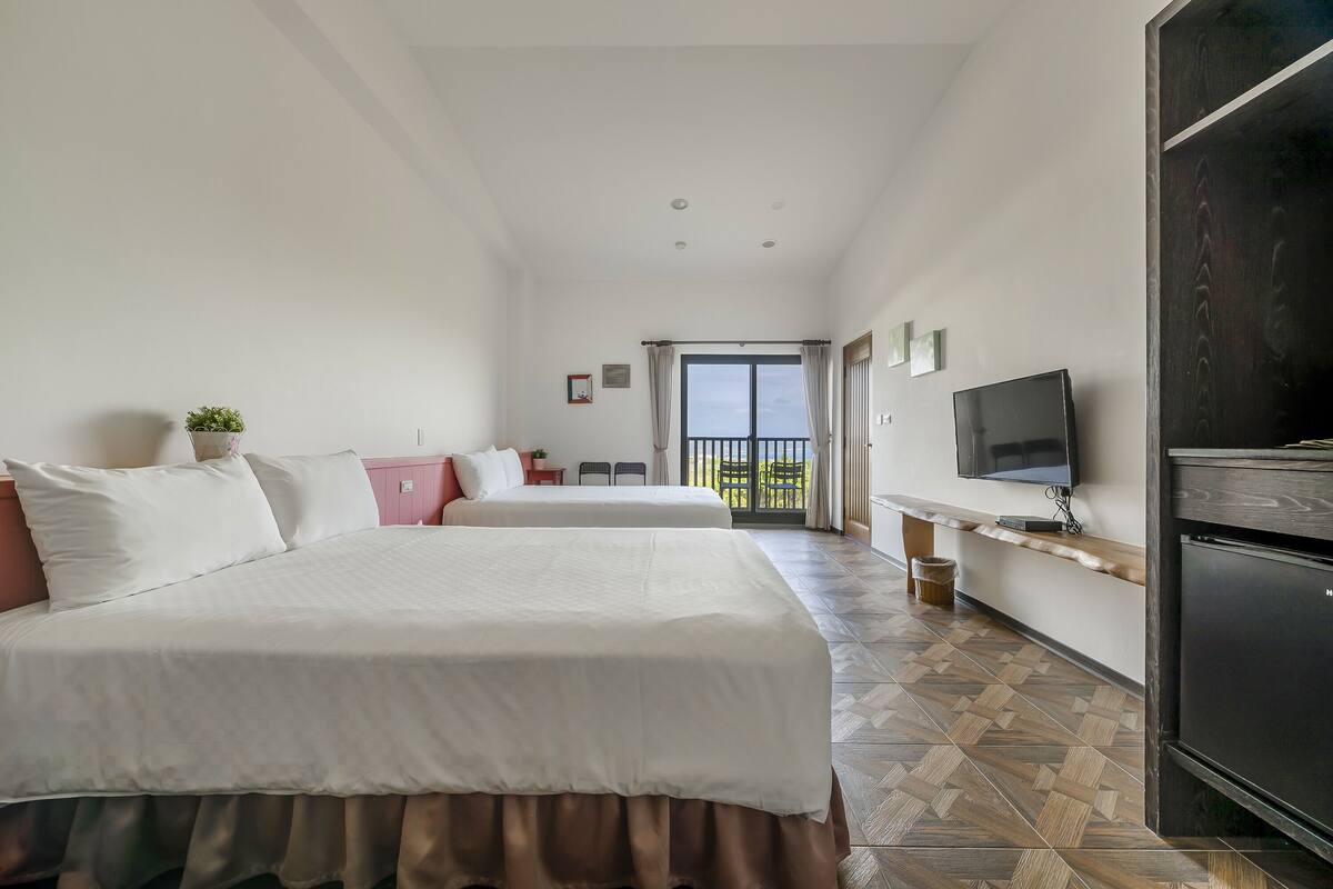 A hotel room with two beds, a TV, a balcony, and a wooden cabinet.