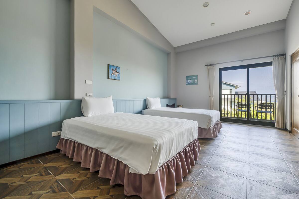 A hotel room with two beds, a large sliding glass door to a balcony, and a view of the outdoors.