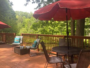 A wooden deck with outdoor furniture, including chairs and a table, and a red umbrella providing shade.