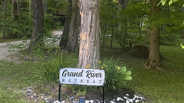 Señal para Grand River Retreat en un área boscosa con un camino de piedra y vegetación.