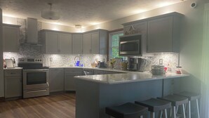 Una cocina moderna con gabinetes grises, una isla central con taburetes altos, electrodomésticos de acero inoxidable y un salpicadero con diseño de espiga.