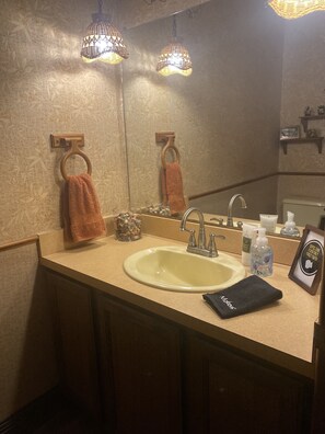 A bathroom with a sink, mirror, towel rings, and a framed sign.