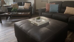 Una sala de estar con un sofá de cuero marrón oscuro, un reposapiés a juego y una mesa de centro con una planta en maceta.