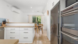 Une cuisine moderne avec des meubles blancs, un four encastré et un coin repas comprenant une table et des chaises en bois.
