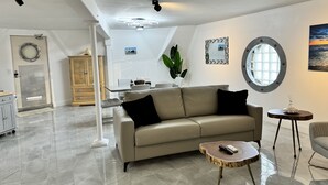 Amplia sala de estar con un sofá moderno, una mesa de centro y un comedor con una mesa y sillas blancas.
