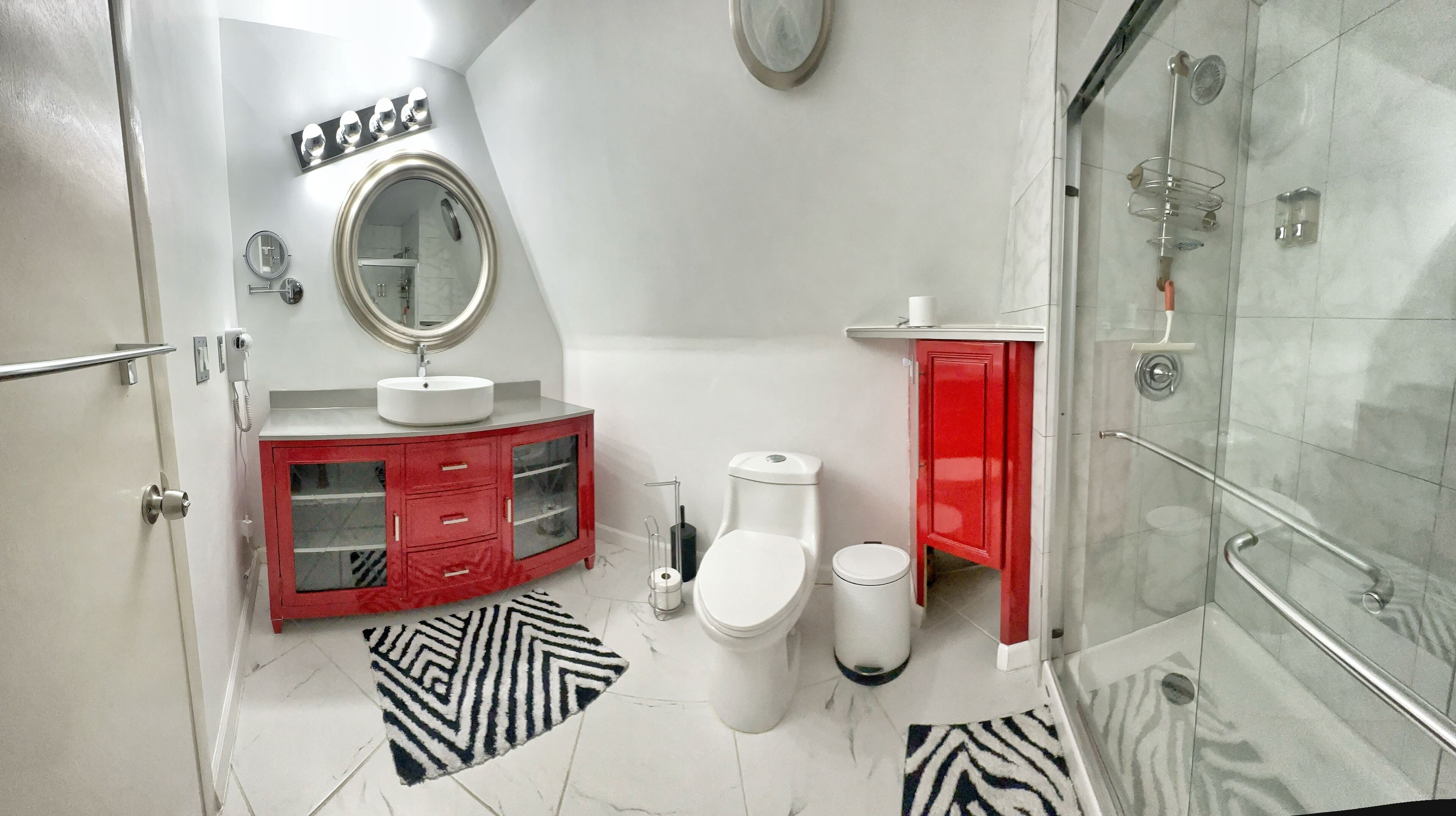 A bathroom with a white sink, a toilet, a shower, and a red cabinet.