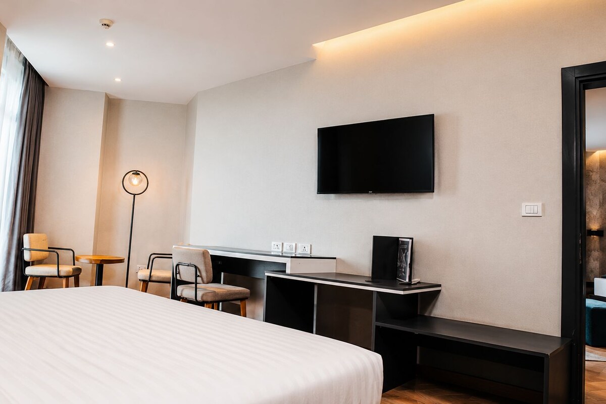 Habitación de hotel con una cama grande, un escritorio, televisor de pantalla plana, una silla y una lámpara de pie.