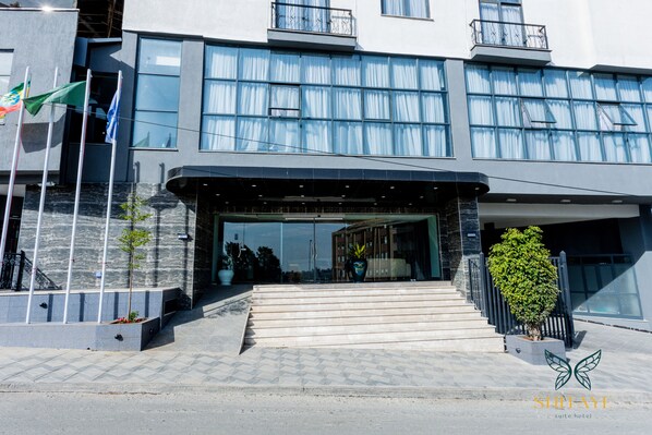 A modern hotel entrance with a glass facade, a covered entrance, and a staircase leading up. - Shitaye Suite Hotel (Addis Ababa)