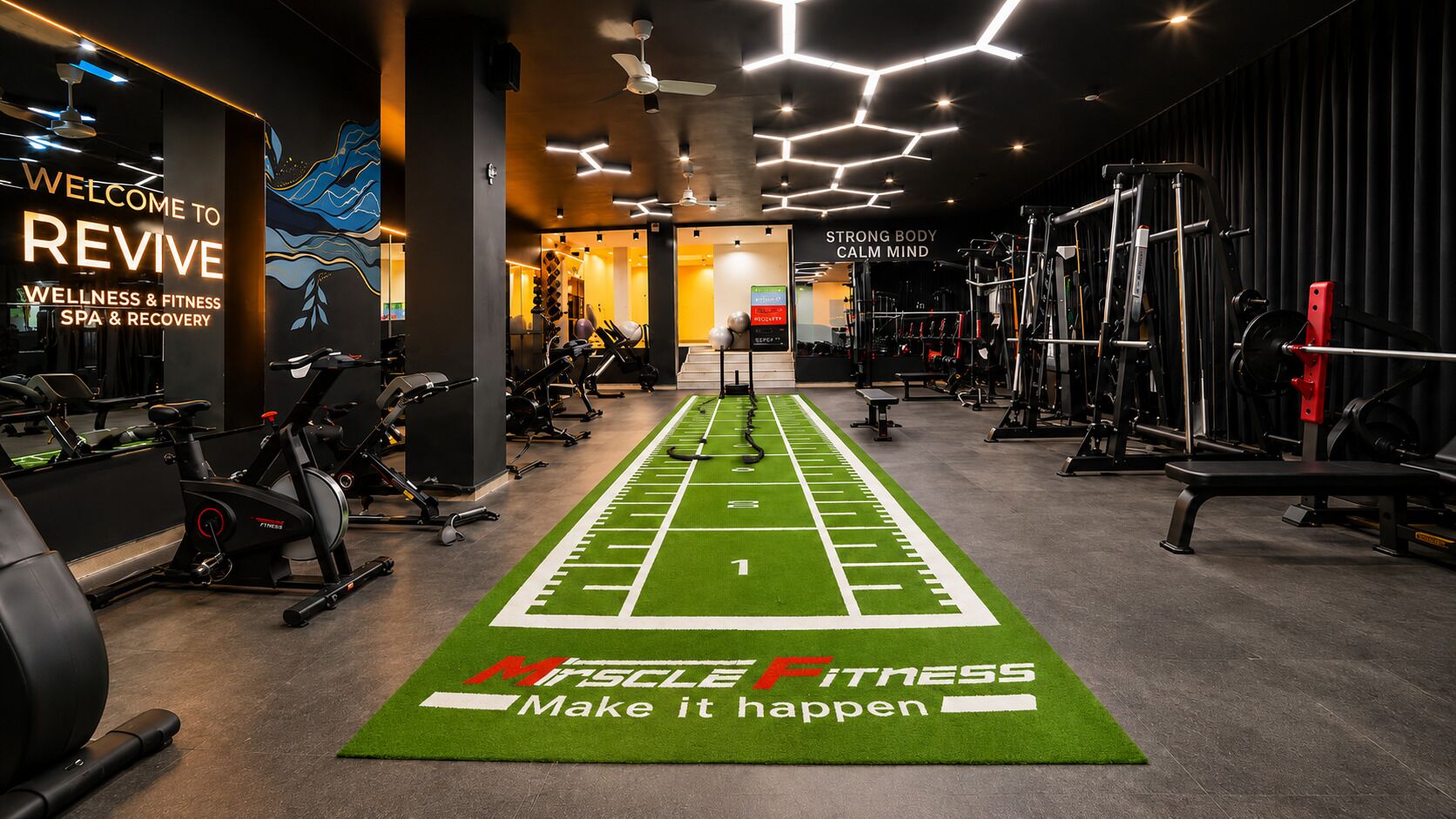 A gym with a green turf running track, exercise equipment, and motivational wall art.