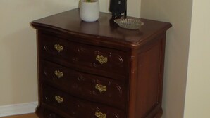 Eine Holzkommode mit drei Schubladen, eine Topfpflanze, eine Lampe und eine kleine dekorative Schale darauf.