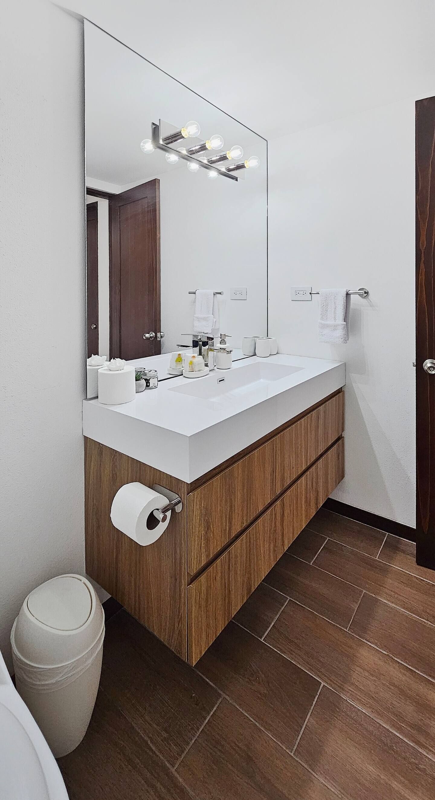 A modern bathroom with a white sink, wooden vanity, and a large mirror with lights.
