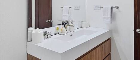 A modern bathroom with a white sink, wooden vanity, and a large mirror with lights.
