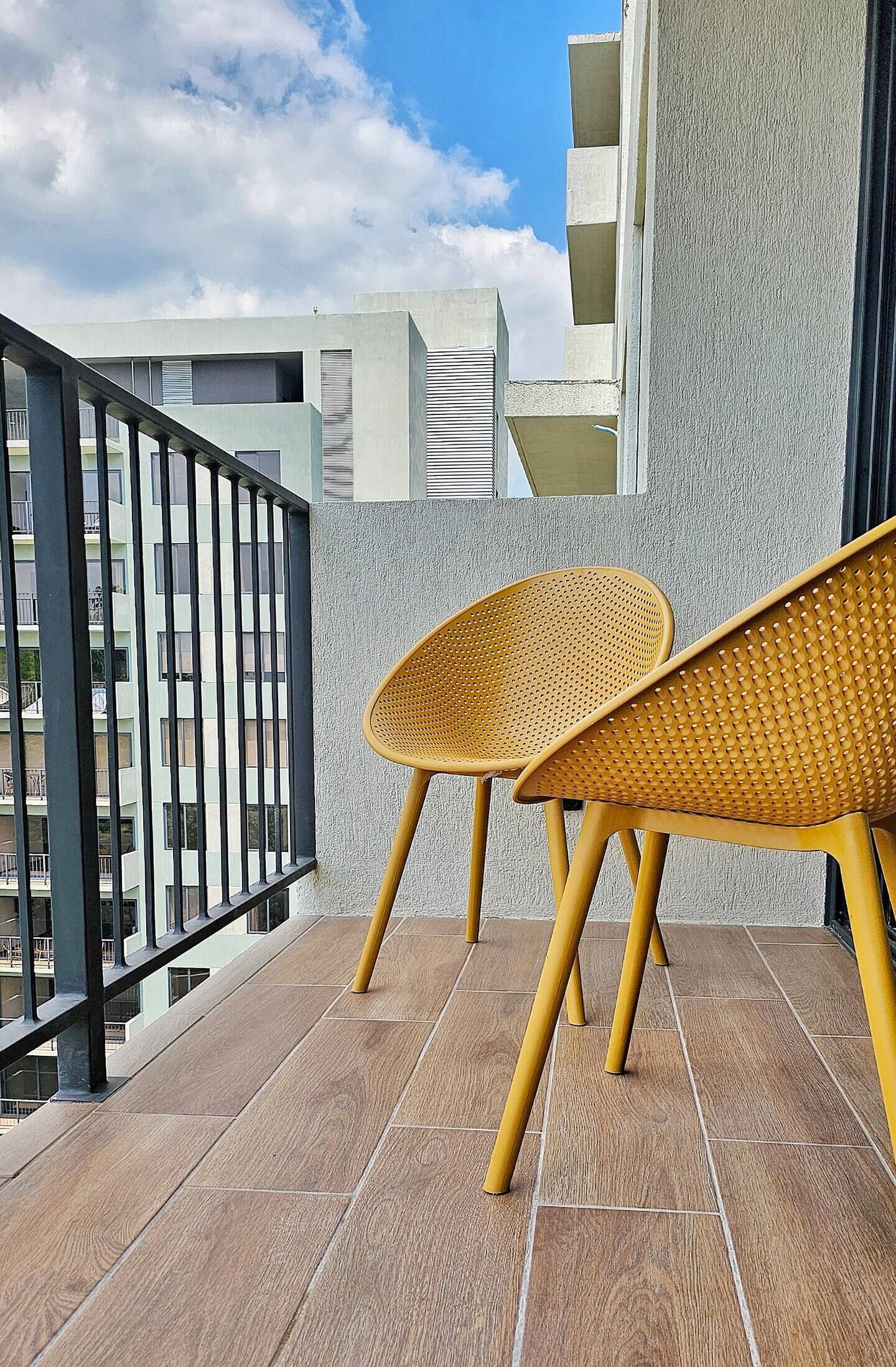 Ein Balkon mit zwei Korbstühlen, einem Metallgeländer und Blick auf ein Gebäude mit Balkonen.