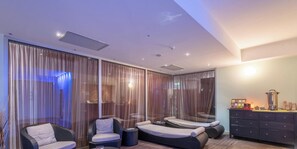 Un espacio lounge moderno con mobiliario de mimbre, una estación de café y ventanas amplias con cortinas translúcidas.