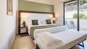 A hotel room with a double bed, a smaller bed, a nightstand with a lamp, a framed picture, and a view of the outside. - Hotiday Otranto Centro Storico (Otranto)