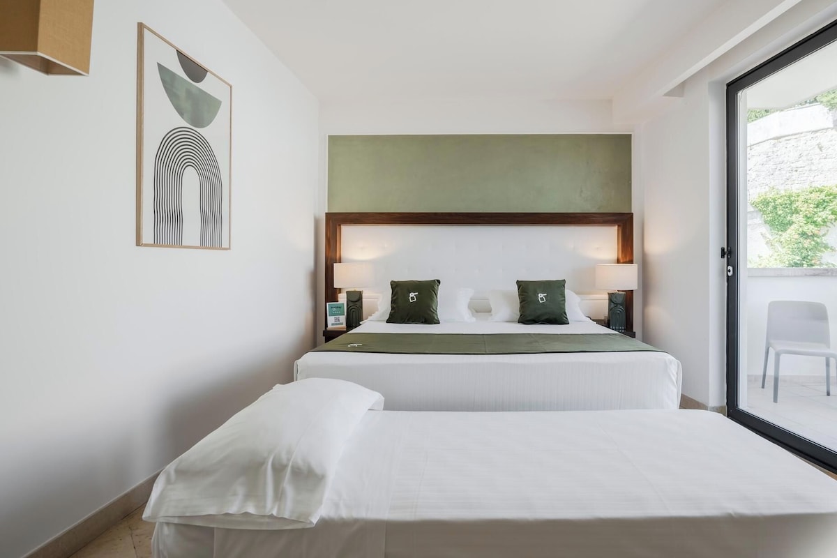 A hotel room with two beds, a large window, and a green accent wall.