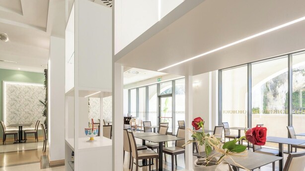 A modern dining area with tables and chairs, large windows, and a view of the outdoors. - Hotiday Otranto Centro Storico (Otranto)