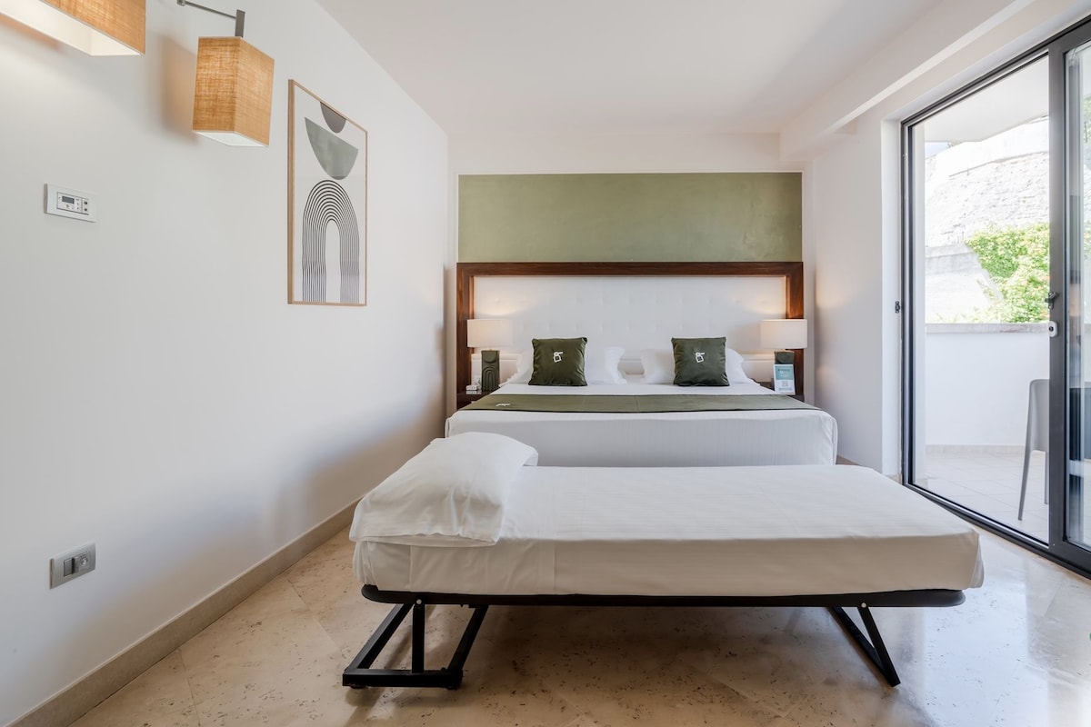 Habitación de hotel con dos camas, un ventanal grande y vista a zonas verdes.