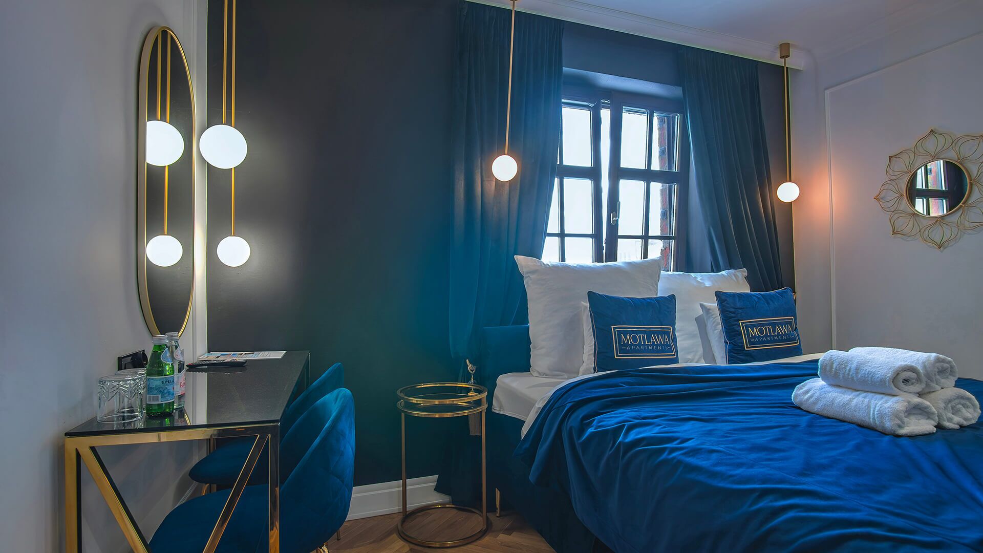 Ein Hotelzimmer mit Bett, Schreibtisch, Stuhl, Spiegel und einem Fenster mit Vorhängen.