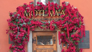 A building entrance with a sign reading "MOTLAWAS APARTMENTS" surrounded by vibrant red flowers. - Motlawa Apartments - Old Town by the river, Fast Wifi (Gdansk)